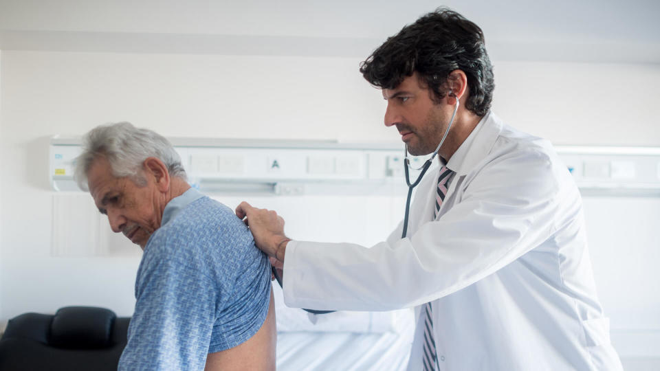 Doctor doing his medical rounds at the hospital listening to a senior patients lungs.