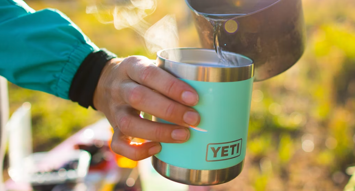 hand holding yeti tumbler travel mug outside with hot water pouring into it