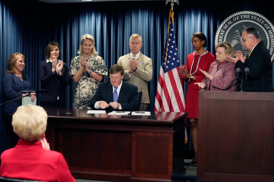 Mississippi Gov. Tate Reeves is surrounded by applauding lawmakers and others as he signs bills that are intended to improve the foster care system, speed up adoptions and provide tax credits for donations to pregnancy resource centers on Wednesday, April 19, 2023, at a state office building in Jackson, Miss.