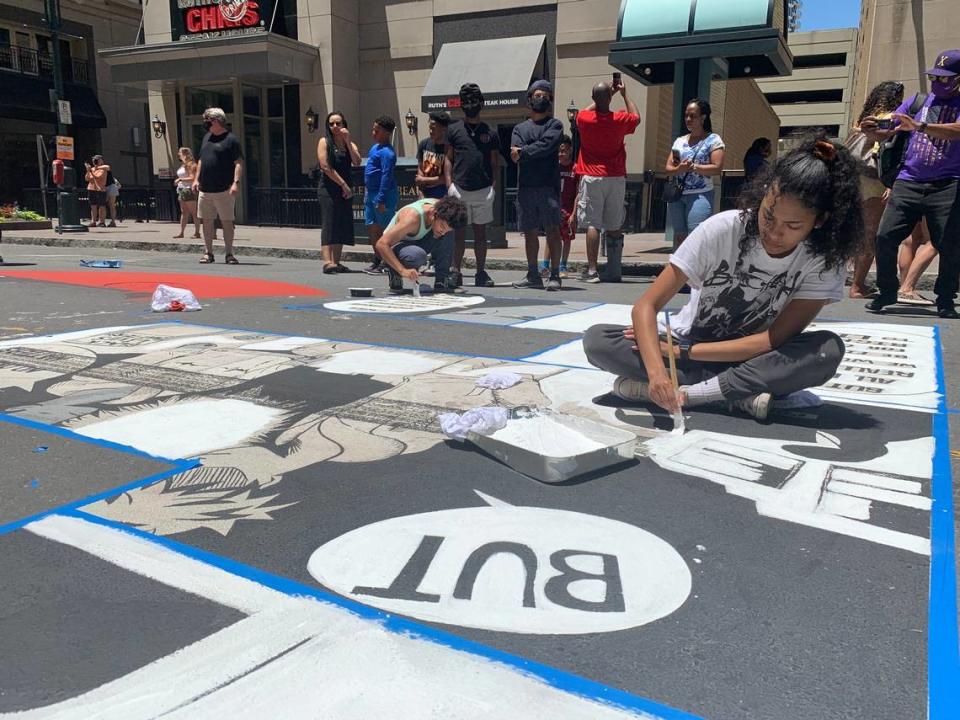 Kiana Mui works to repair her letter, which she originally painted as part of the Black Lives Matter mural on Tryon Street in uptown Charlotte in June 2020. The mural had been defaced by tire tracks.