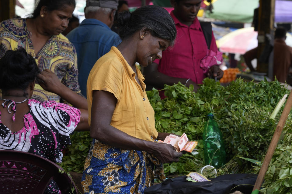 A vendor counts currency notes as she sells vegetables at a market place in Colombo, Sri Lanka, Thursday, June. 1, 2023. The Central Bank of Sri Lanka reduced its interest rates Thursday, June 1, 2023, for the first time since the island nation declared bankruptcy last year. Stern fiscal controls, improved foreign currency income and help from an International Monetary Fund program has resulted in inflation slowing faster than expected. (AP Photo/Eranga Jayawardena)