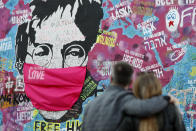 FILE - A couple look at the "Lennon Wall" with a face mask attached to the image of John Lennon, in Prague, Czech Republic, on April 6, 2020. An album, "Gimme Some Truth" by John Lennon, will be released Friday, on what would have been his 80th birthday. (AP Photo/Petr David Josek, File)