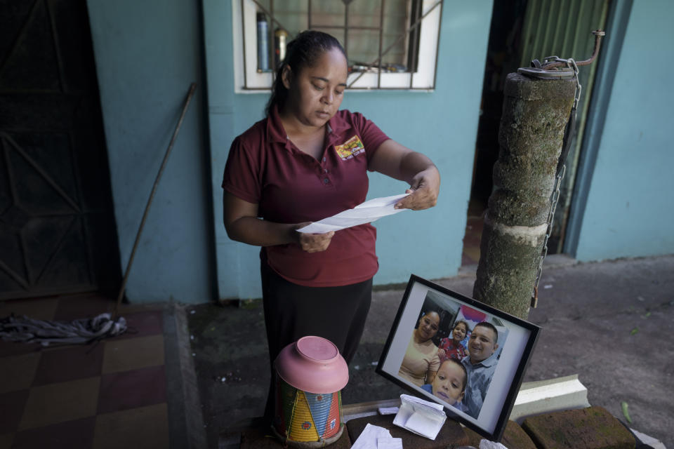 Nancy Cruz de Quintanilla looks over documents regarding the detention and death of her late husband Jose Mauricio Quintanilla Medrano, pictured in the family portrait nearby, in San Miguel, El Salvador, Thursday, Oct. 13, 2022. Her husband, a local small businessman and part-time evangelical preacher, was detained under the "state of exception" after a tip about a suspicious person in a neighborhood that was not his own. Days later he was bused to the Mariona prison where he reportedly died of a pulmonary edema. (AP Photo/Moises Castillo)