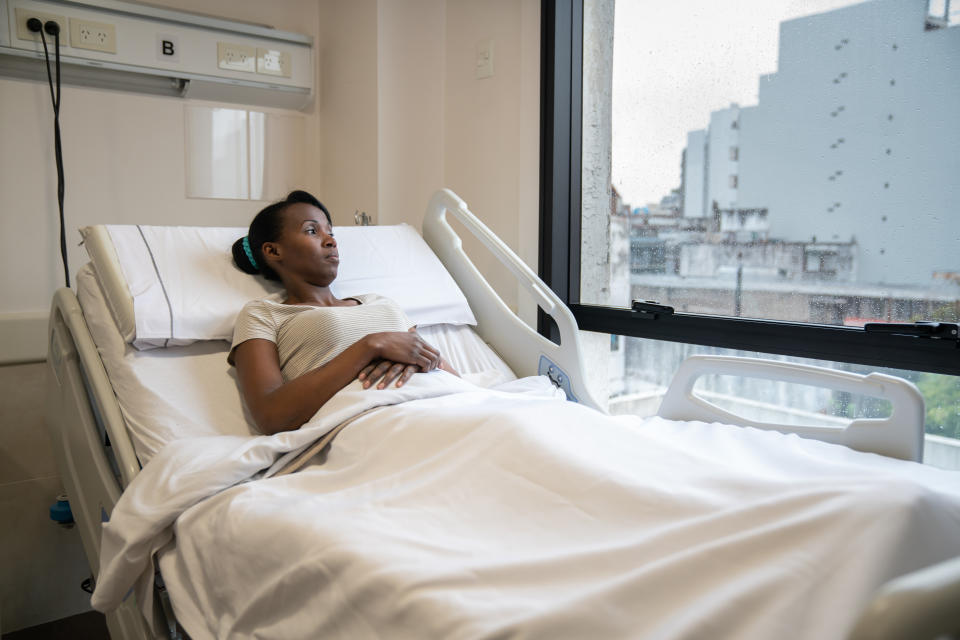 Black young woman lying down on hospital bed looking at window very pensive - Healthcare concepts