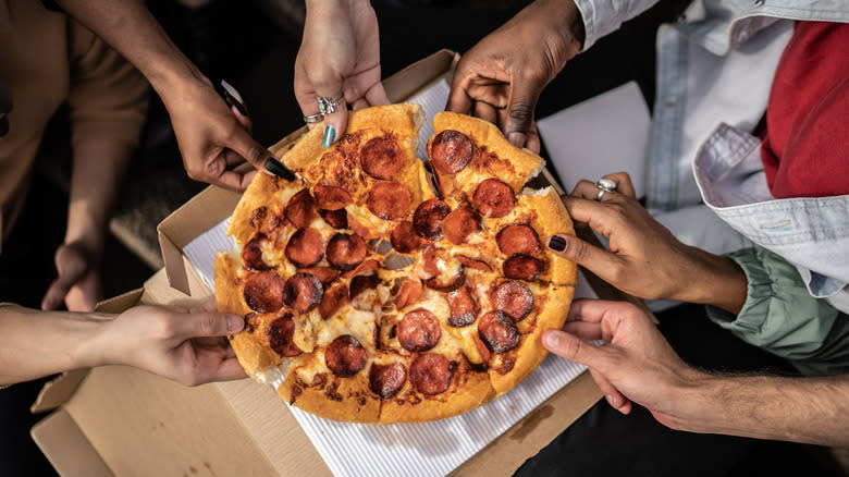 group of friends pulling apart pizza