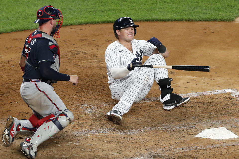 Atlanta Braves catcher Tyler Flowers, left, watches as New York Yankees Luke Voit falls to the dirt after being hit on the hand by a pitch during the fifth inning of a baseball game, Tuesday, Aug. 11, 2020, in New York. Voit was seen by a trainer but stayed in the game. (AP Photo/Kathy Willens)