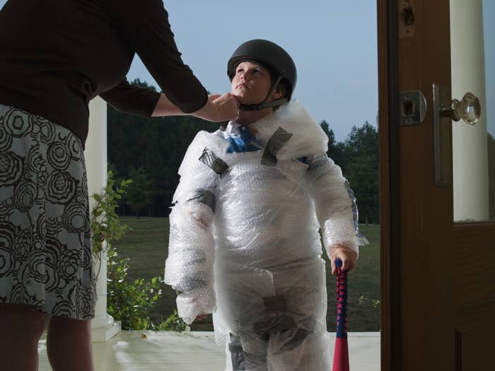 A woman fastening her son's helmet as he's covered head-to-toe in plastic padding.