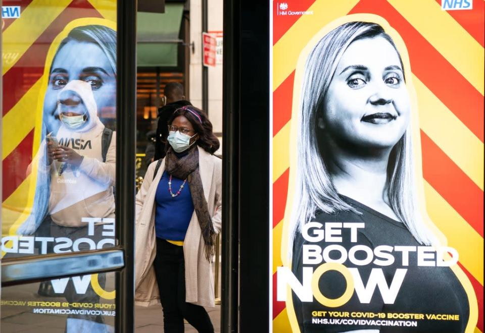 People wearing face masks walk past a UK Government advert encouraging people to book a Covid booster (Dominic Lipinski/PA) (PA Wire)