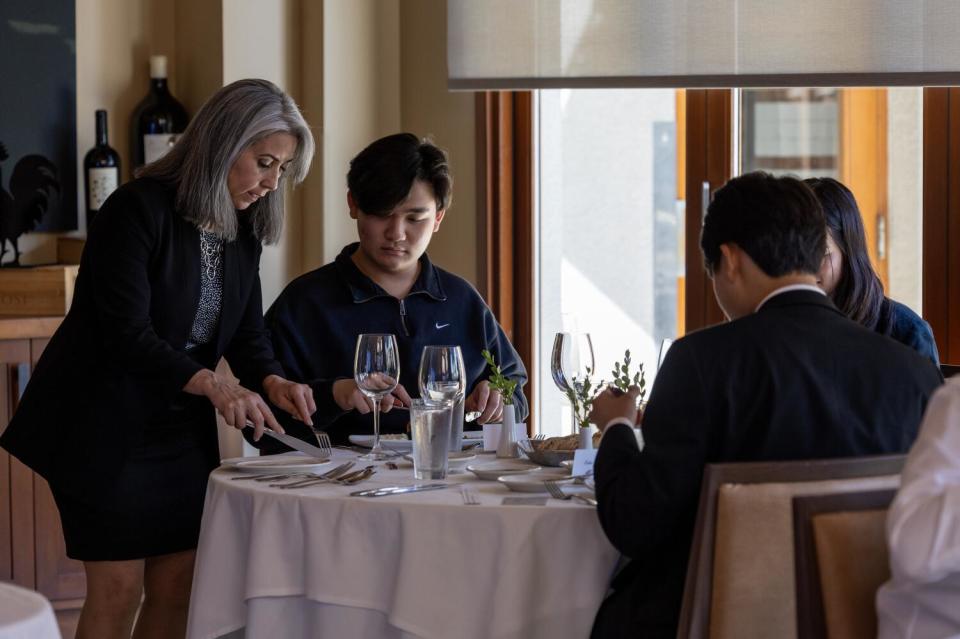 A woman teaches a young man the proper way to hold utensils