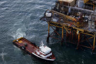 In this aerial photograph, a supply vessel moves near an oil rig in the Gulf of Mexico damaged by an explosion and fire, Friday, Nov. 16, 2012, about 25 miles southeast of Grand Isle, La. Four people were transported to a hospital with critical burns and two were missing. (AP Photo/Gerald Herbert)