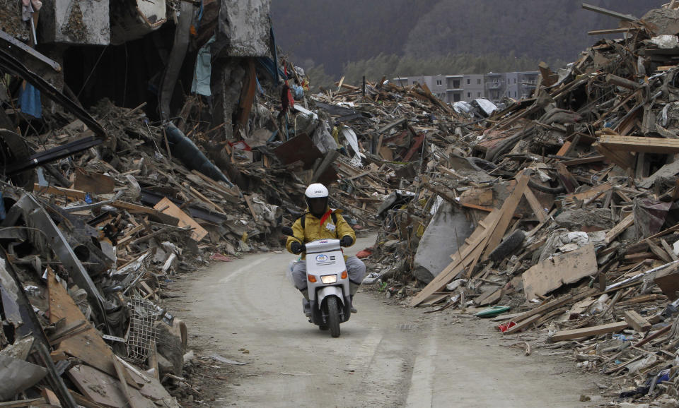 FILE - A man rides his motorcycle on a makeshift road amid rubble in Rikuzentakata, Iwate Prefecture, northern Japan, on March 20, 2011, after the March 11 earthquake and tsunami devastated the area. The 2011 quake, tsunami and nuclear meltdown in northern Japan provides a glimpse of what Turkey and Syria could face in the years ahead. No two events are alike, but the recent disaster resembles Japan's in the sheer enormity of the psychological trauma, of the loss of life and of the material destruction. (AP Photo/Shizuo Kambayashi, File)