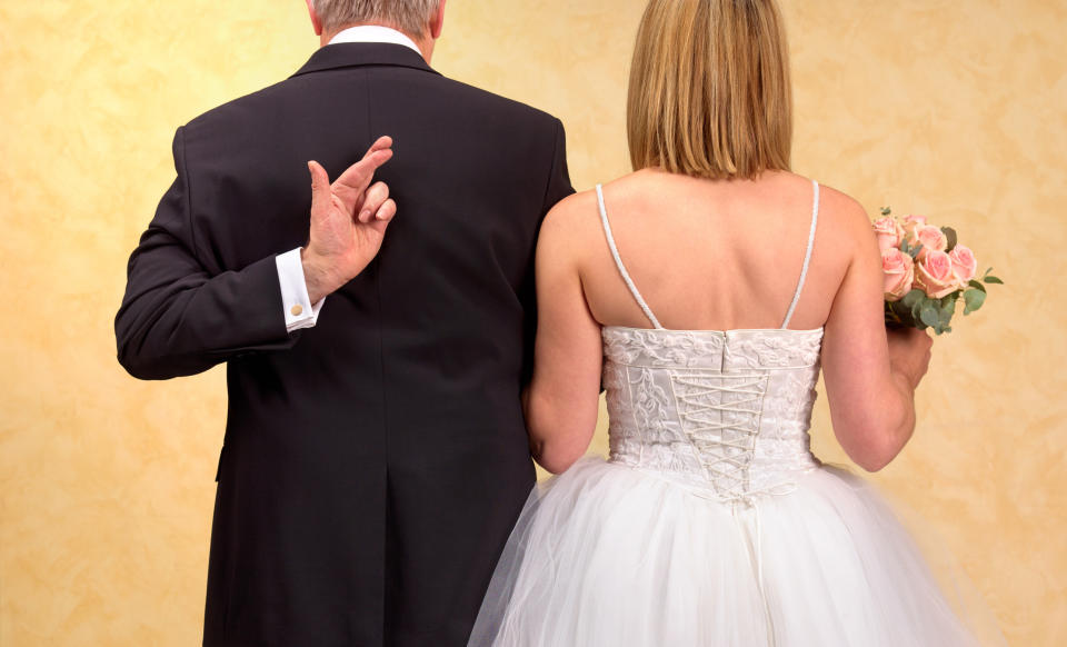 Bride in a lace-up gown and groom with crossed fingers behind his back