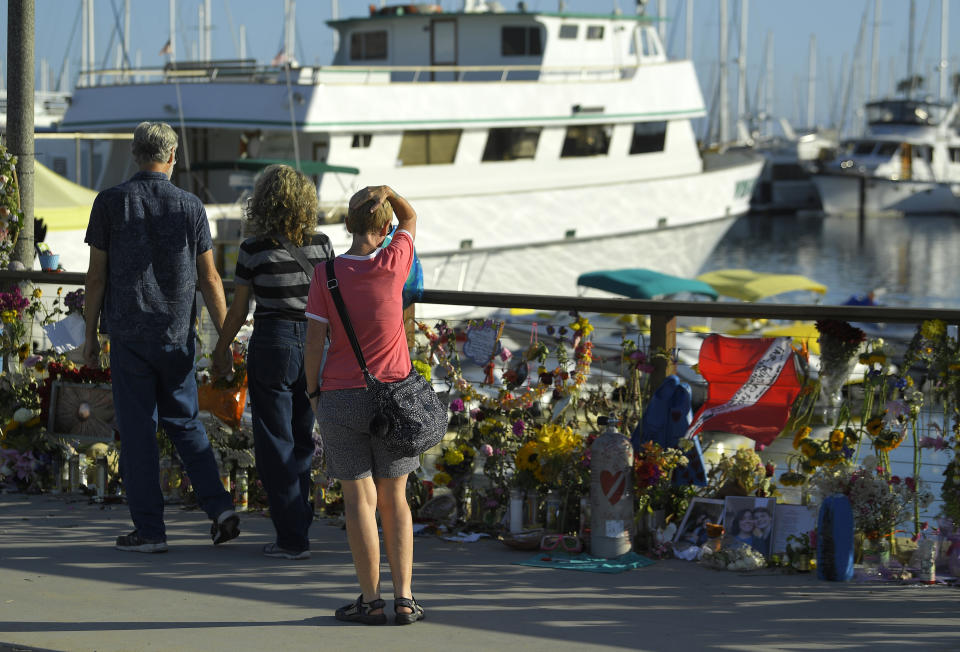 FILE - In this Sept. 6, 2019, file photo, people visit a growing memorial to the victims who died aboard the dive boat Conception as its sister boat Vision sits in the background, in Santa Barbara, Calif. The captain of a scuba diving boat that burned and sank off the California coast, killing 34 people below deck, has pleaded not guilty to federal manslaughter charges. Jerry Boylan surrendered Tuesday, Feb. 16, 2021, and was arraigned in Los Angeles federal court on 34 counts of seaman's manslaughter. (AP Photo/Mark J. Terrill, File)