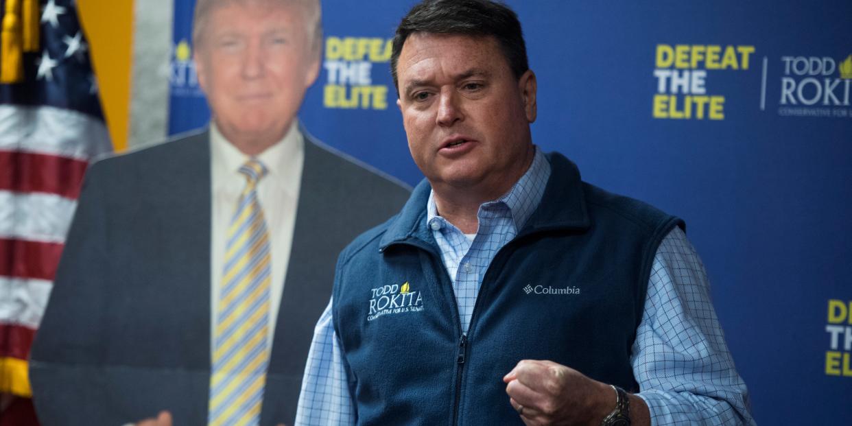 Todd Rokita campaigning in a vest next to a US flag and cardboard cutout of Donald Trump