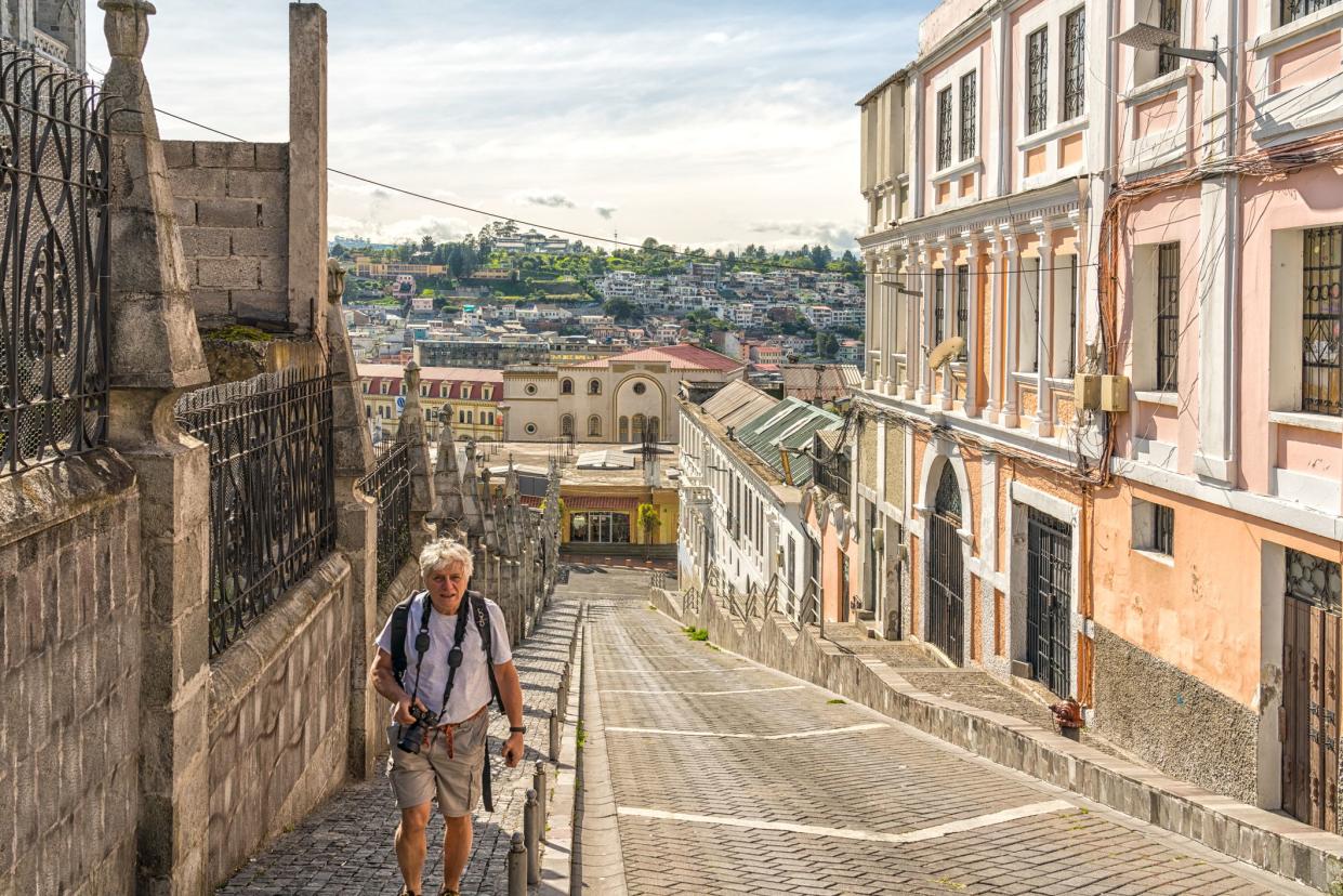 senior men with photo camera going up a steep street in old town of Quito, Ecuador