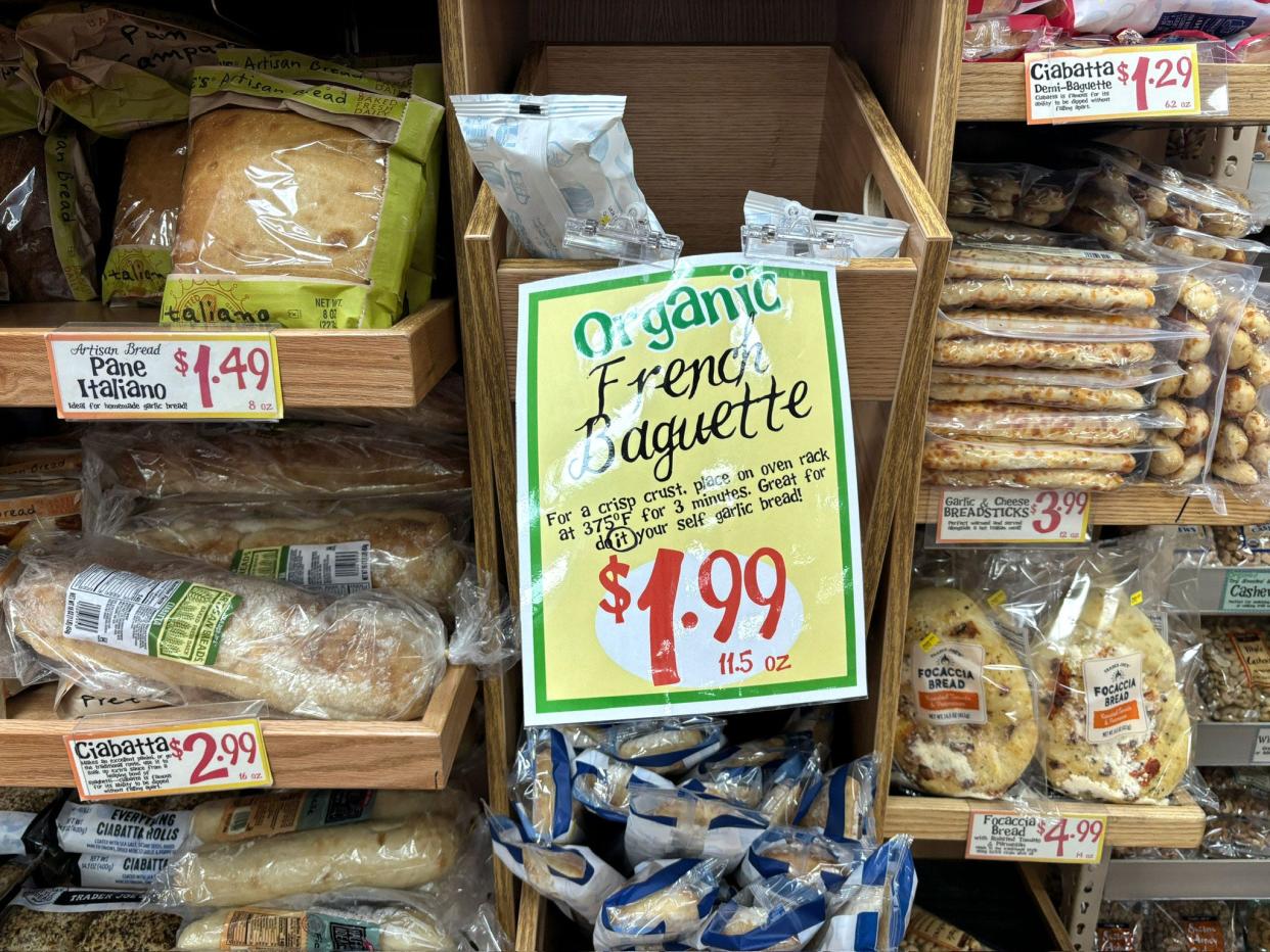 Different kinds of bread on display at Trader Joe's. The largest sign in the middle reads, "Organic French baguette $1.99." 