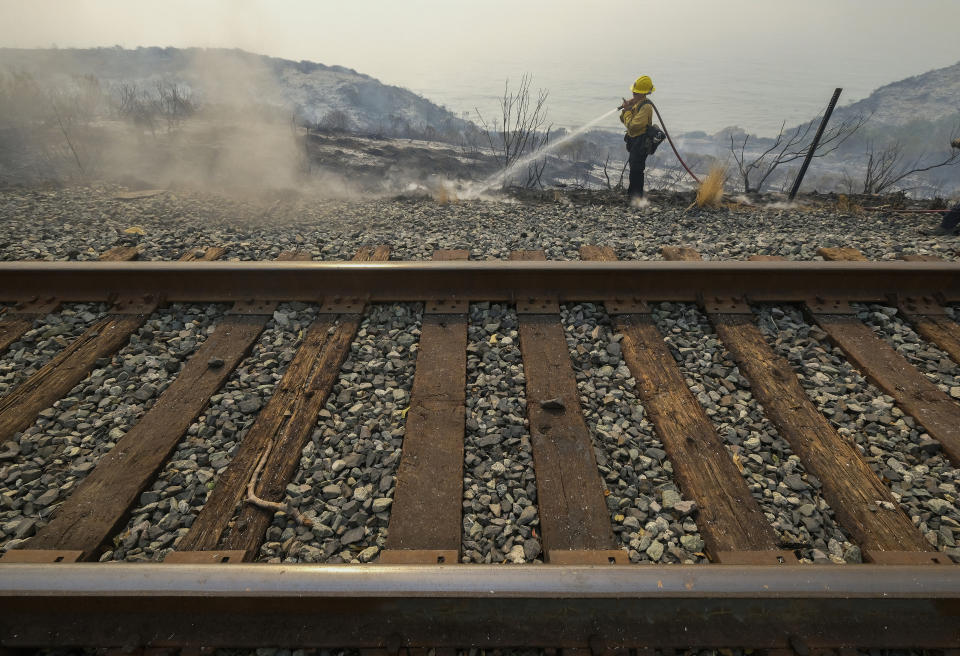 County of Santa Barbara Fire Department firefighters extinguish a roadside fire next to train tracks off of the U.S. 101 highway Wednesday, Oct. 13, 2021, in Goleta, Calif. A wildfire raging through Southern California coastal mountains threatened ranches and rural homes and kept a major highway shut down Wednesday as the fire-scarred state faced a new round of dry winds that raise risk of flames. The Alisal Fire covered more than 22 square miles (57 square kilometers) in the Santa Ynez Mountains west of Santa Barbara. (AP Photo/Ringo H.W. Chiu)