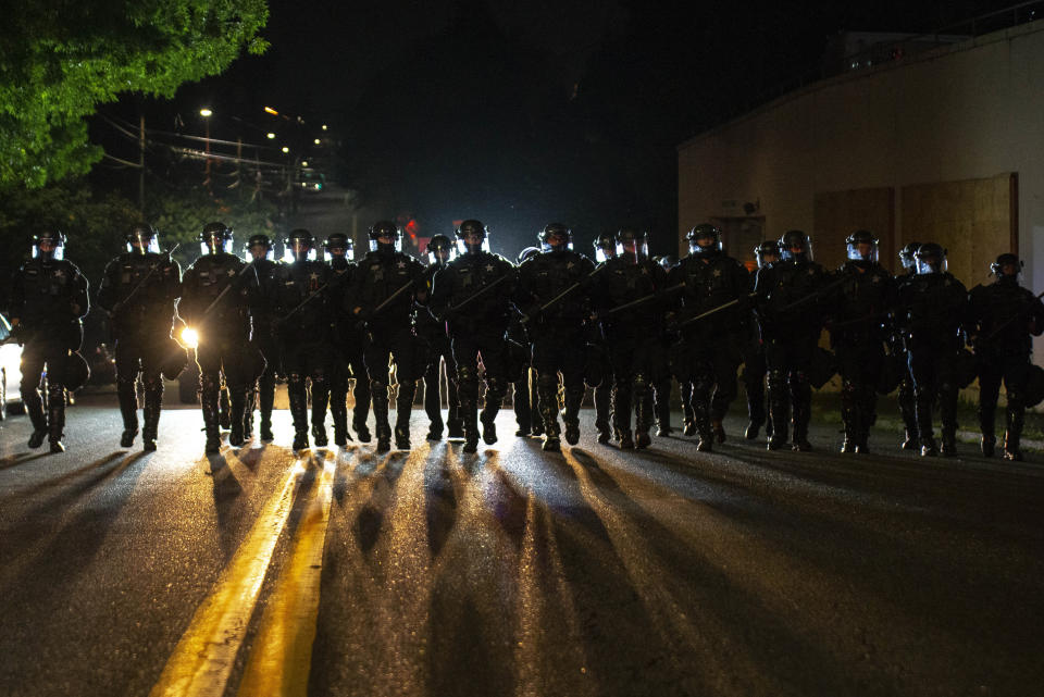 Portland police officers walk through the Laurelhurst neighborhood after dispersing a protest of about 200 people from in front of the Multnomah County Sheriff's Office early in the morning on Saturday, Aug. 8, 2020 in Portland, Ore. (AP Photo/Nathan Howard)