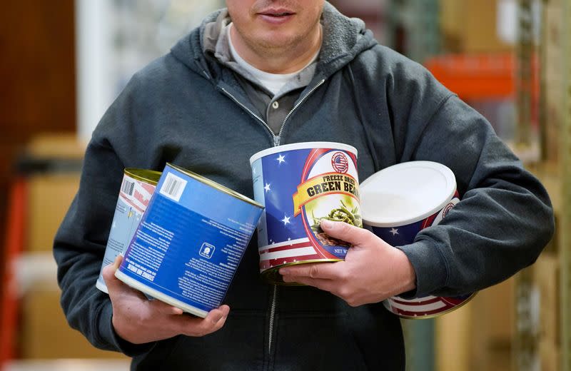 An employee carries cans of freeze dried food to put into boxes as part of personal protection and survival equipment kits ordered by customers preparing against novel coronavirus, at Nitro-Pak in Midway