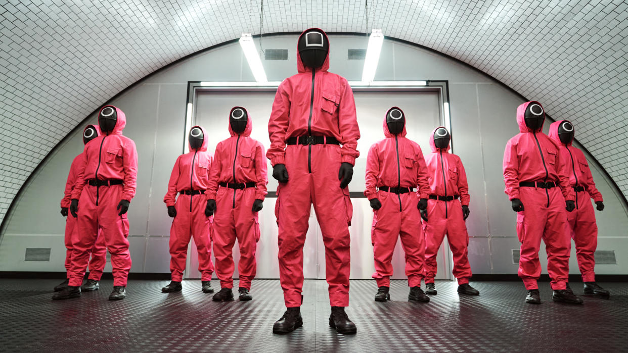  An official screenshot from Netflix's Squid Game TV show of people in pink jumpsuits while wearing black masks 
