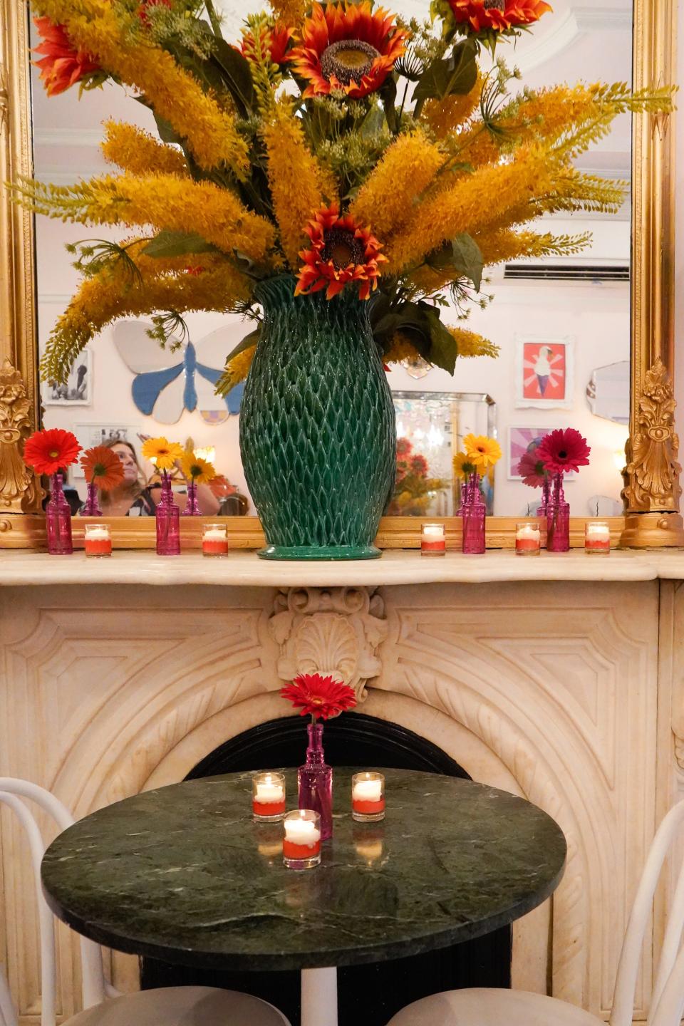 a table setting at Serendipity 3 with three candles on the table and a fireplace with candles and flowers in front of a mirror on  the mantle