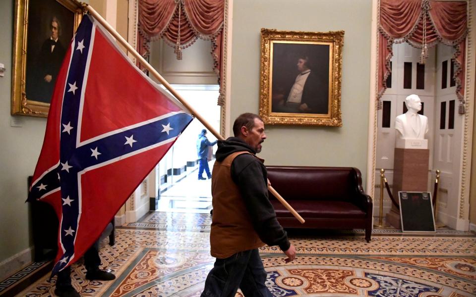 A supporter of Donald Trump wanders the second floor of the Senate holding a Confederate flag - Reuters