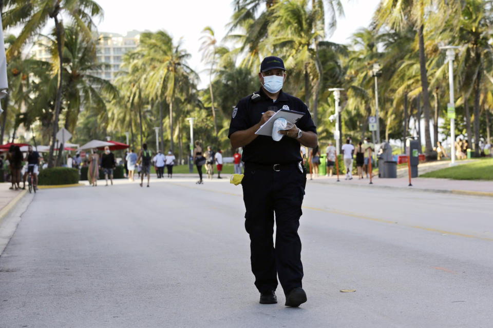 Luis Negron, a Miami Beach code compliance officer, walks along Ocean Drive amid the coronavirus pandemic, Friday, July 24, 2020, in Miami Beach, Fla. Masks are mandated both indoors and outdoors in Miami Beach. People found not wearing a mask are subject to a civil fine of $50. (AP Photo/Lynne Sladky)