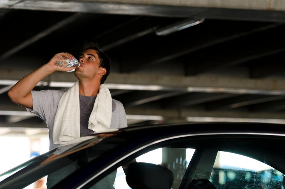 man standing outside of his car cooling off with towel and water bottle