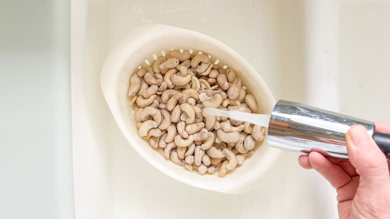 Rinsing and draining soaked cashews in colander