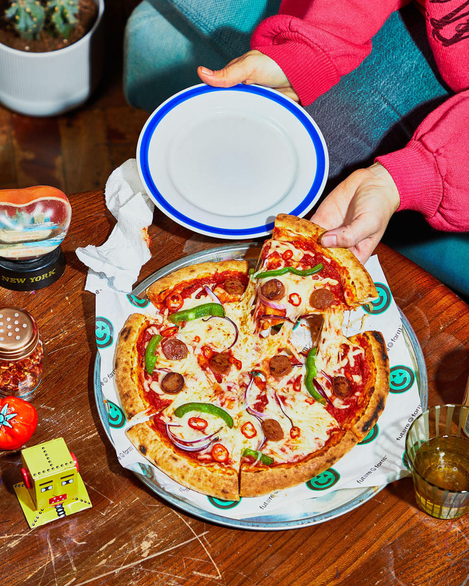 A picture of a vegan pizza on a table, someone is grabbing a slice