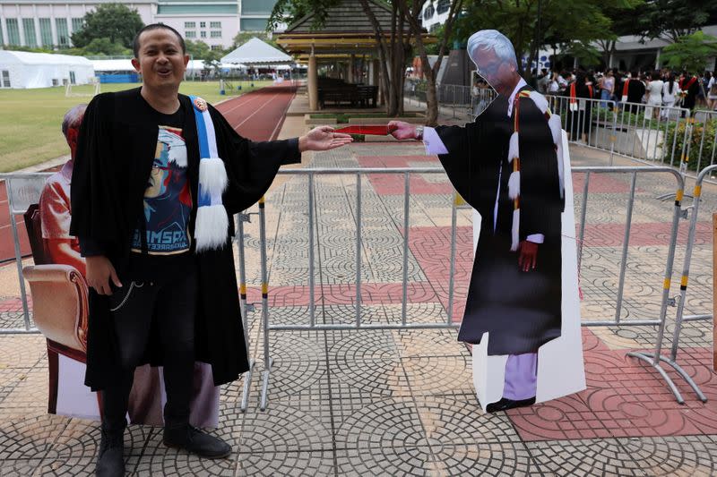 A student stands next to a cardboard figure of Somsak Jeamteerasakul, a Thai academic exiled, before his graduation ceremony, as some students have boycotted the ceremony because it is led by King Maha Vajiralongkorn, at Thammasat University in Bangkok