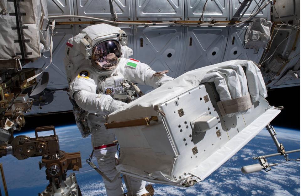 an astronaut in a spacesuit handles a large piece of machinery while in space