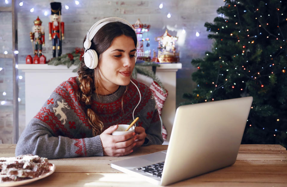 Woman with cup of coffee using laptop and headphones at Christmas time. (Getty Images)