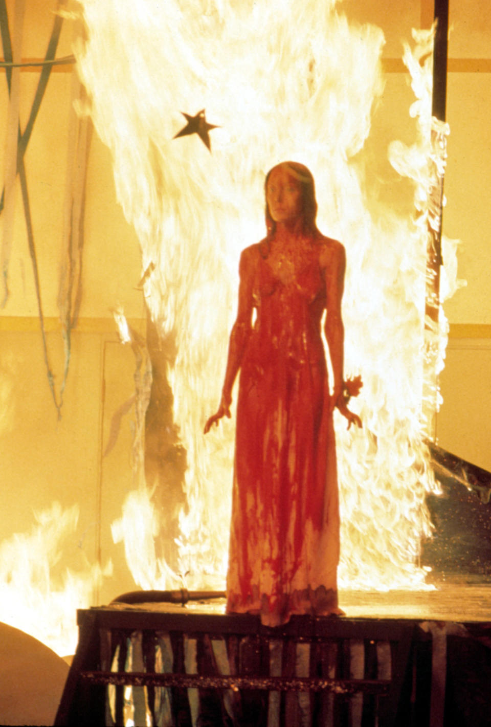 Carrie, drenched in blood, with fire behind her