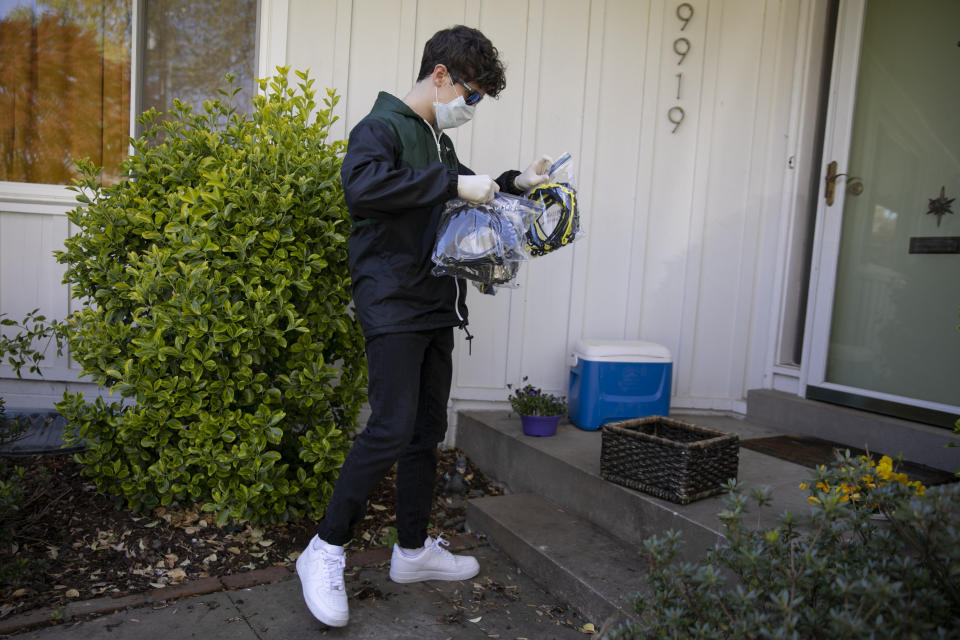 High school junior, Will Olsen, 17, of Kensington, Md., picks up bags holding pieces for medical face shields that were printed using personal 3D printers, in Kensington, Md., Sunday, April 19, 2020. He then delivered the bags to the Eaton Hotel in downtown Washington for assembly. (AP Photo/Jacquelyn Martin)