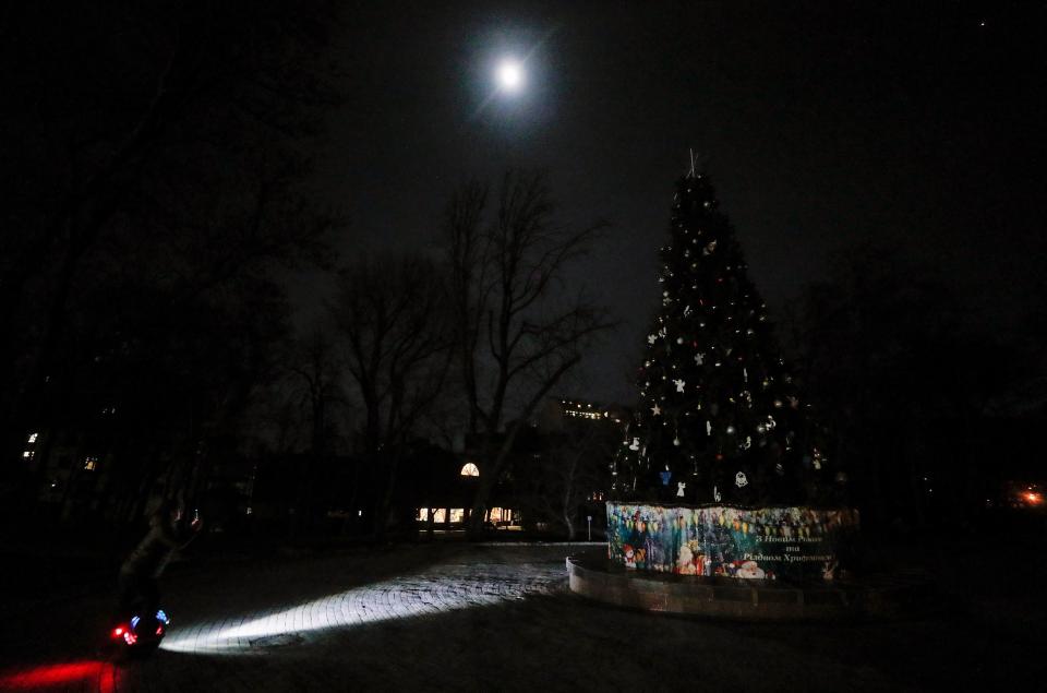 A man takes pictures by phone as he rides an electric unicycle past a dark Christmas tree in downtown Kyiv last night (EPA)