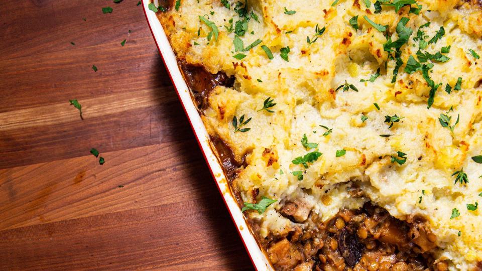 piece of vegan shepherds pie on a blue plate next to a baking dish full of vegan shepherds pie