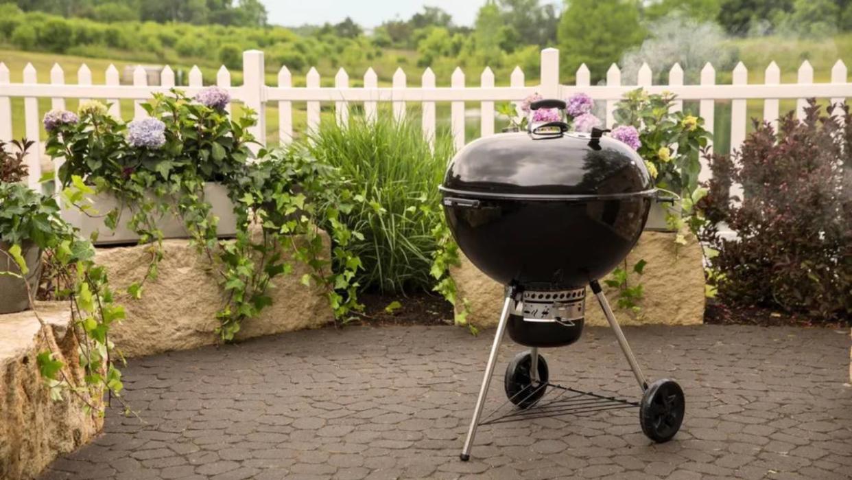  Lifestyle image of the Weber Master-Touch Charcoal BBQ 67cm sitting on a patio in a garden. 