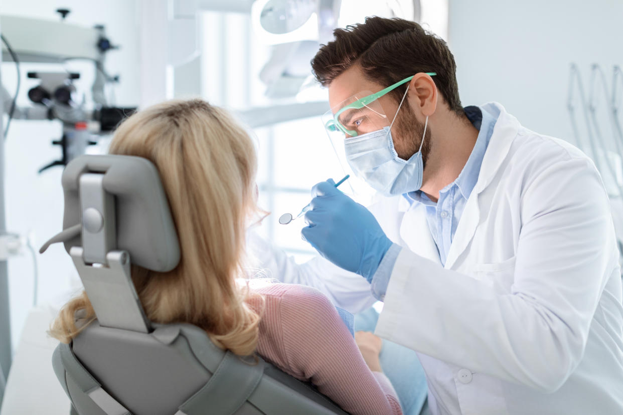Man dentist in face mask and glasses doing treatment for patient blonde lady, holding dental tools, wearing rubber gloves. Stomatology, dentistry, modern dental clinic concept