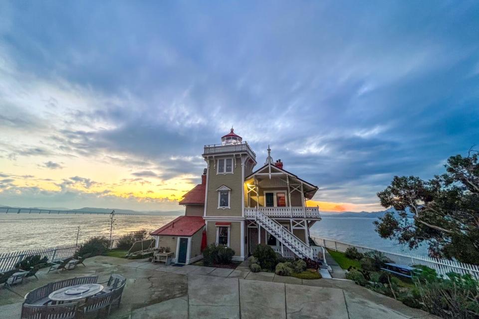 A Victorial lighthouse and building at dusk, under dramatically lit clouds