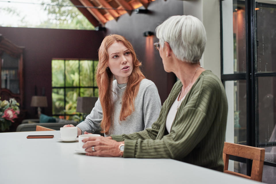 Two women, likely family, engaged in a serious conversation at a table with coffee mugs