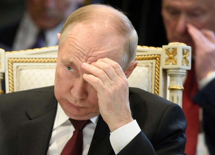 President Vladimir Putin, seated in a gilded chair, raises his hand to his forehead and looks downbeat.