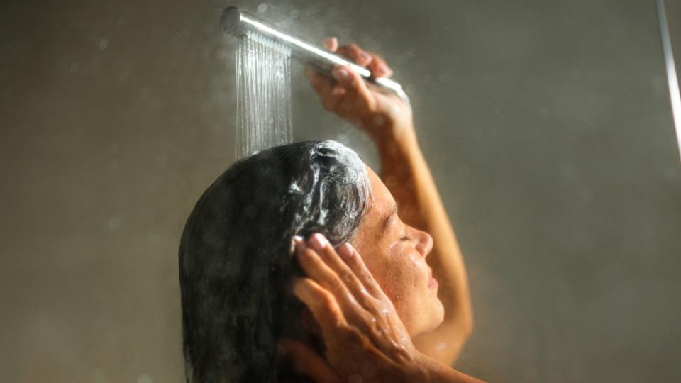Woman seen washing her hair with shampoo and a silver showerhead
