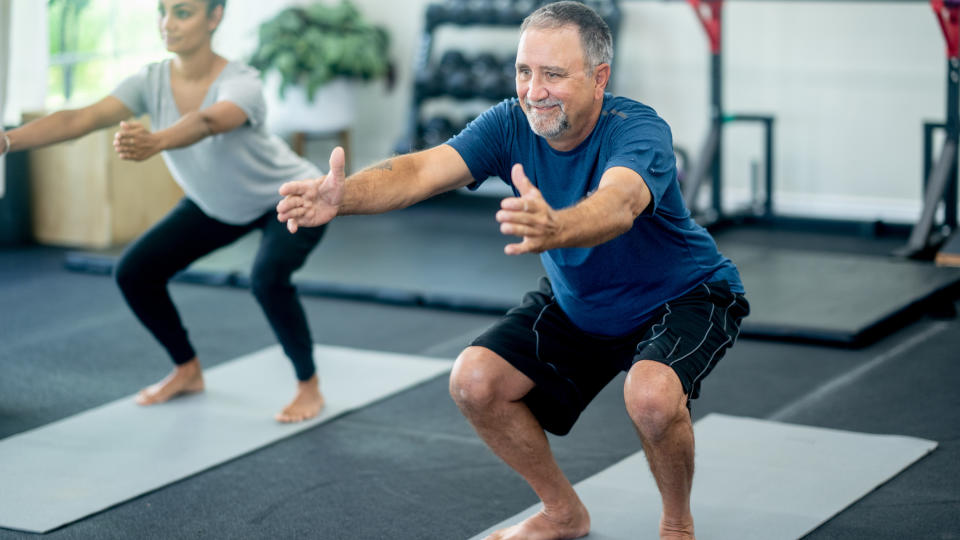 Man and woman on yoga mats in gym doing squats