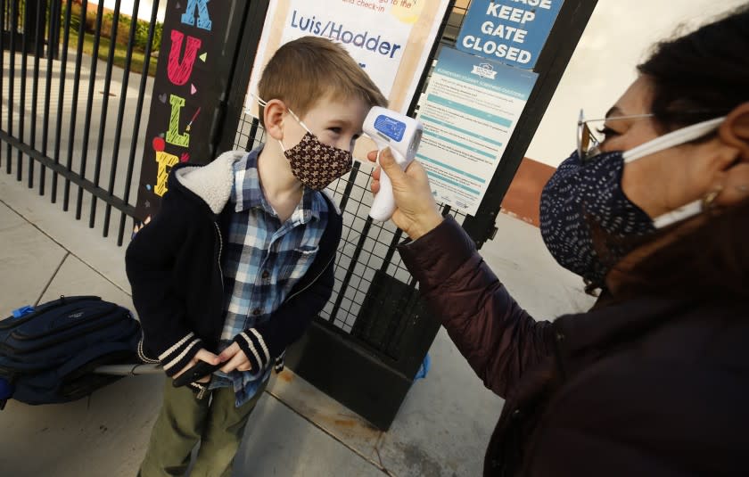 REDONDO BEACH, CA - FEBRUARY 02: First grade student Felix Fuchs has his temperature taken by teachers aide Firoozeh Borjian as he arrives at Alta Vista Elementary School for the second day of classes as Redondo Beach Unified School district has welcomed back some of its K-2 students this week through a waiver. Alta Vista Elementary School on Tuesday, Feb. 2, 2021 in Redondo Beach, CA. (Al Seib / Los Angeles Times).