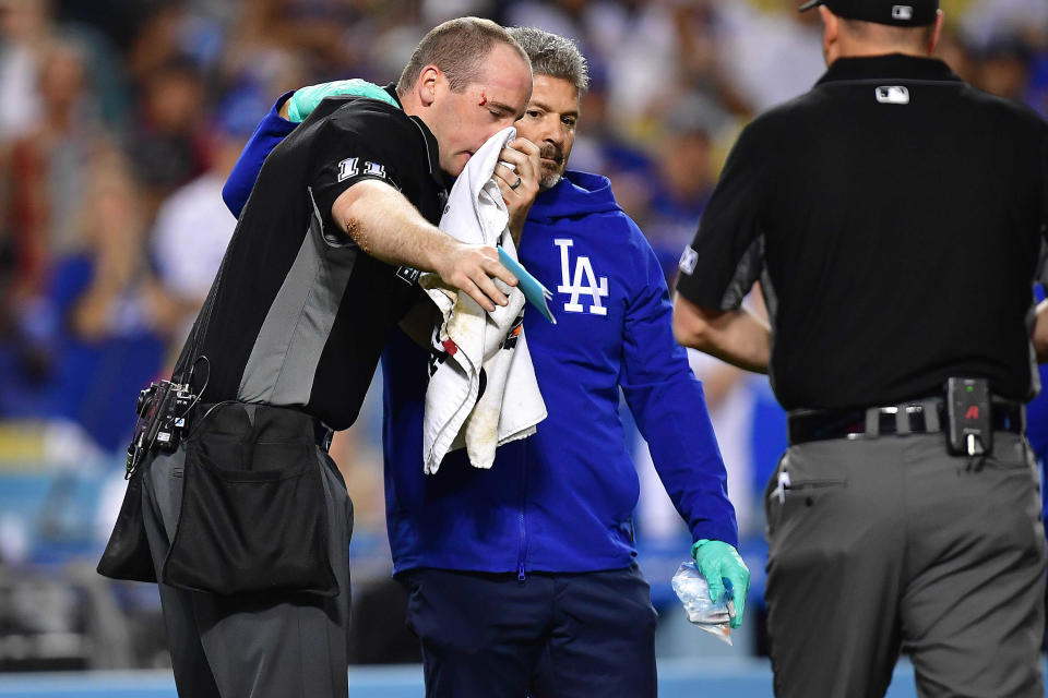 Home plate umpire Nate Tomlinson is helped by Dodgers trainer Nate Lucero after being hit by the bat of Mike Trout.