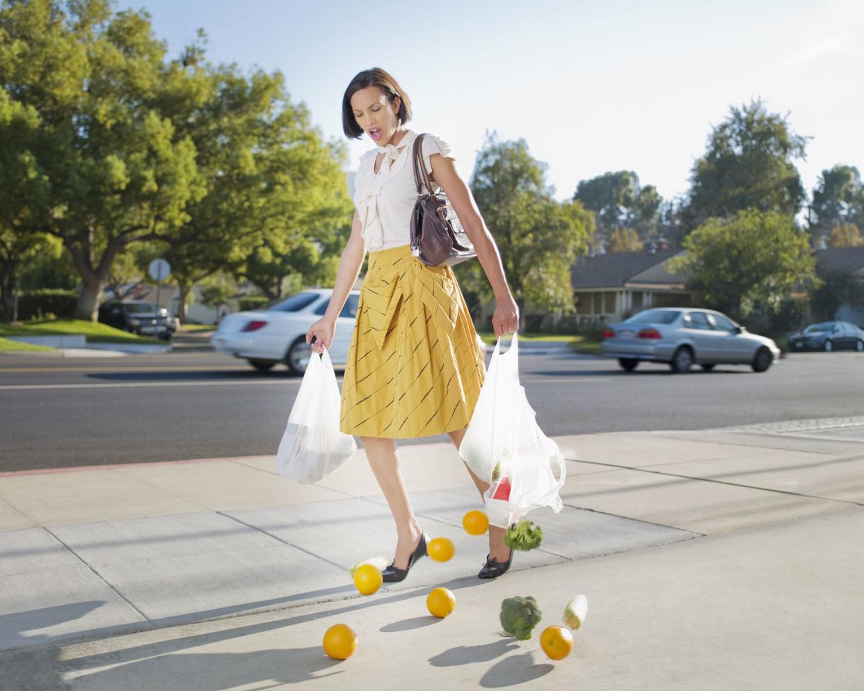 woman dropping groceries on sidewalk because she has a cheap bag