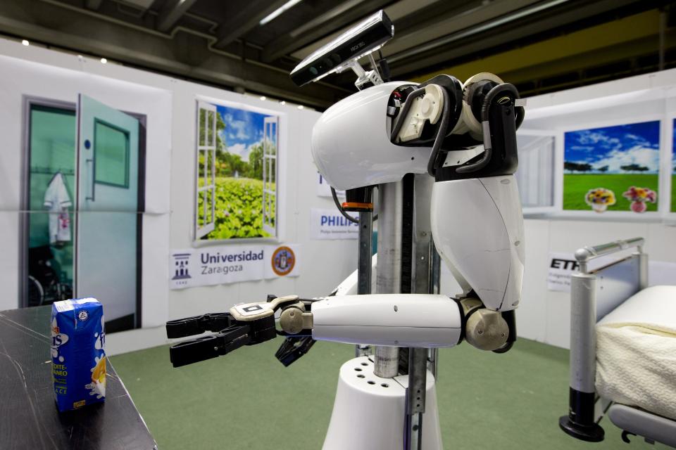 Amigo, a white robot the size of a person, uses information gathered by other robots to move towards a table to pick up a carton of milk and deliver it to an imaginary patient in a mock hospital room at the Technical University of Eindhoven, Netherlands, Wednesday Jan. 15, 2014. A group of five of Europe's top technical universities, together with technology conglomerate Royal Philips NV, are launching an open-source system dubbed "RoboEarth" Thursday. The heart of the mission is to accelerate the development of robots and robotic services via efficient communication with a network, or "cloud". (AP Photo/Peter Dejong)