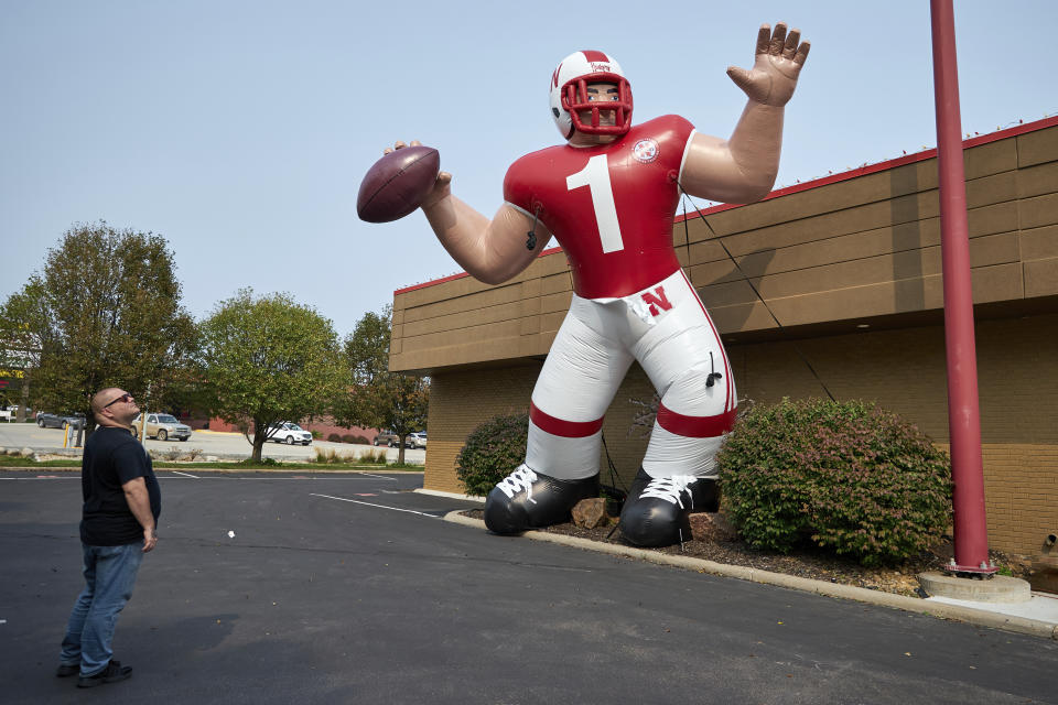 A Nebraska fan stops to look at a giant inflatable football player standing in front of the Husker Hounds sports apparel store in Omaha, Neb., Wednesday, Sept. 16, 2020. It was put up Wednesday after the Big Ten conference changed course Wednesday and said it plans to begin its NCAA college football season the weekend of Oct. 23-24. Each team will have an eight-game schedule. (AP Photo/Nati Harnik)