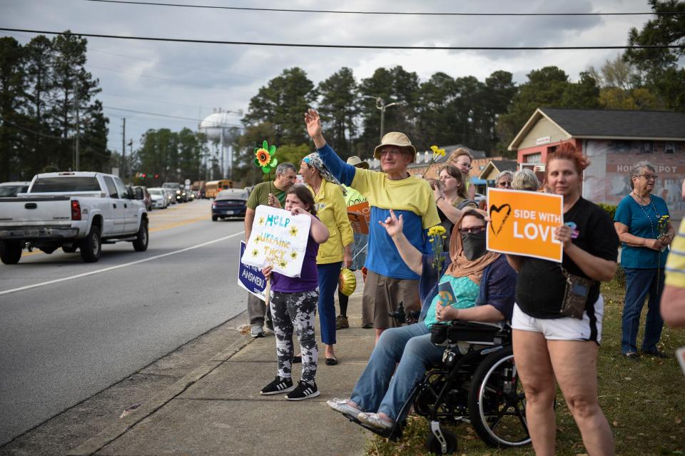 Community members wave to cars during a vigil held for Ukraine off Walton Way Extension on Monday, March 7, 2022. About 50 community members turned out in honor of those in Ukraine. 